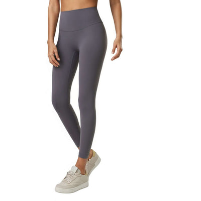 Female model wearing grey, seamless high-waist fitness leggings, standing slightly sideways and leaning forward. Suitable for sports or casual wear.
